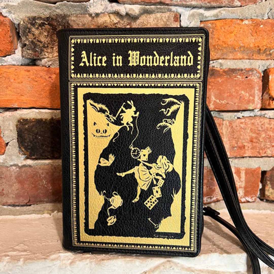 A handbag designed to resemble a book cover with 'Alice in Wonderland' title, featuring a character illustration in black and gold colors.