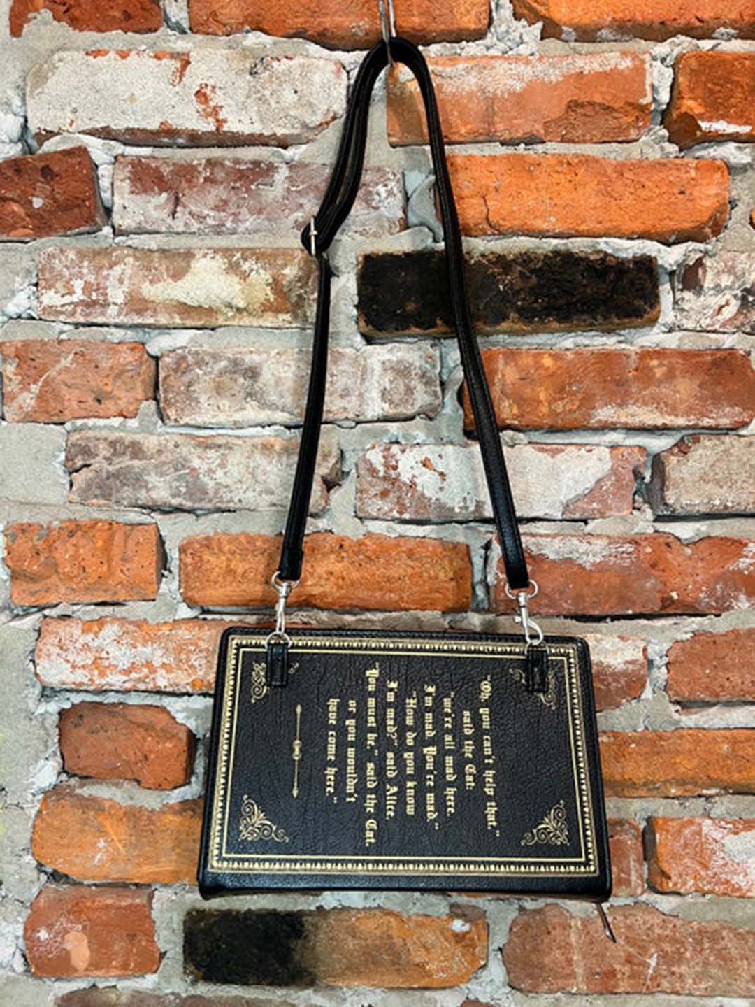 Alice in wonderland storybook purse hanging from crossbody strap against brickwall