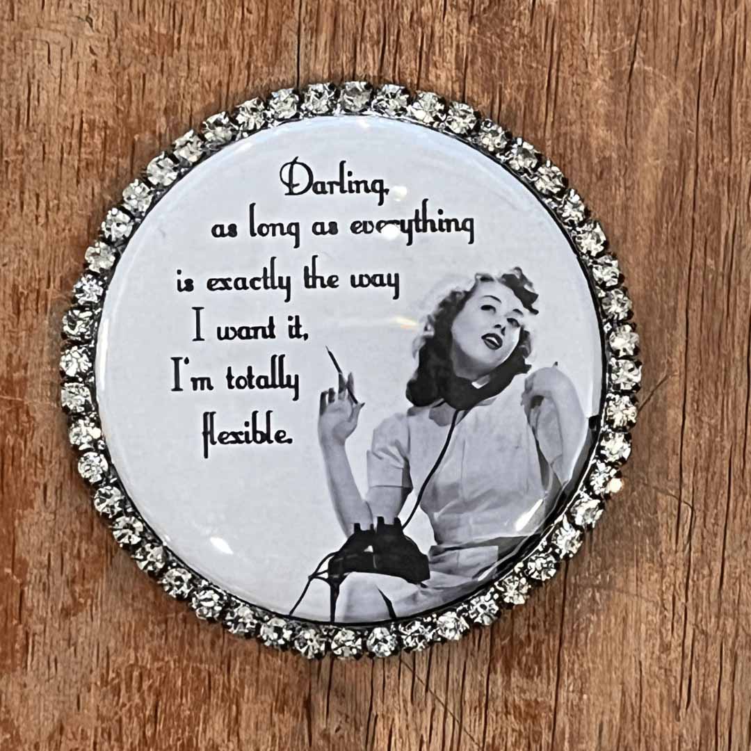 Round decorative magnet with a black and white photo of a woman and text on a wooden surface