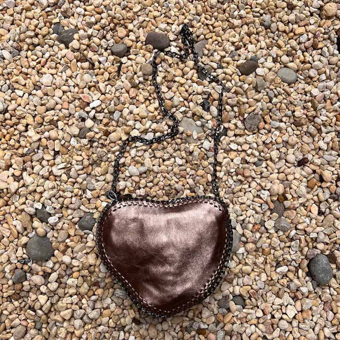 Bronze heart shape purse with chain crossbody strap laying in a bed of stones