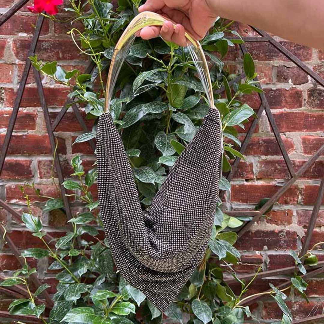 Black Rhinestone bag with faux gold handle against green foliage and brick wall