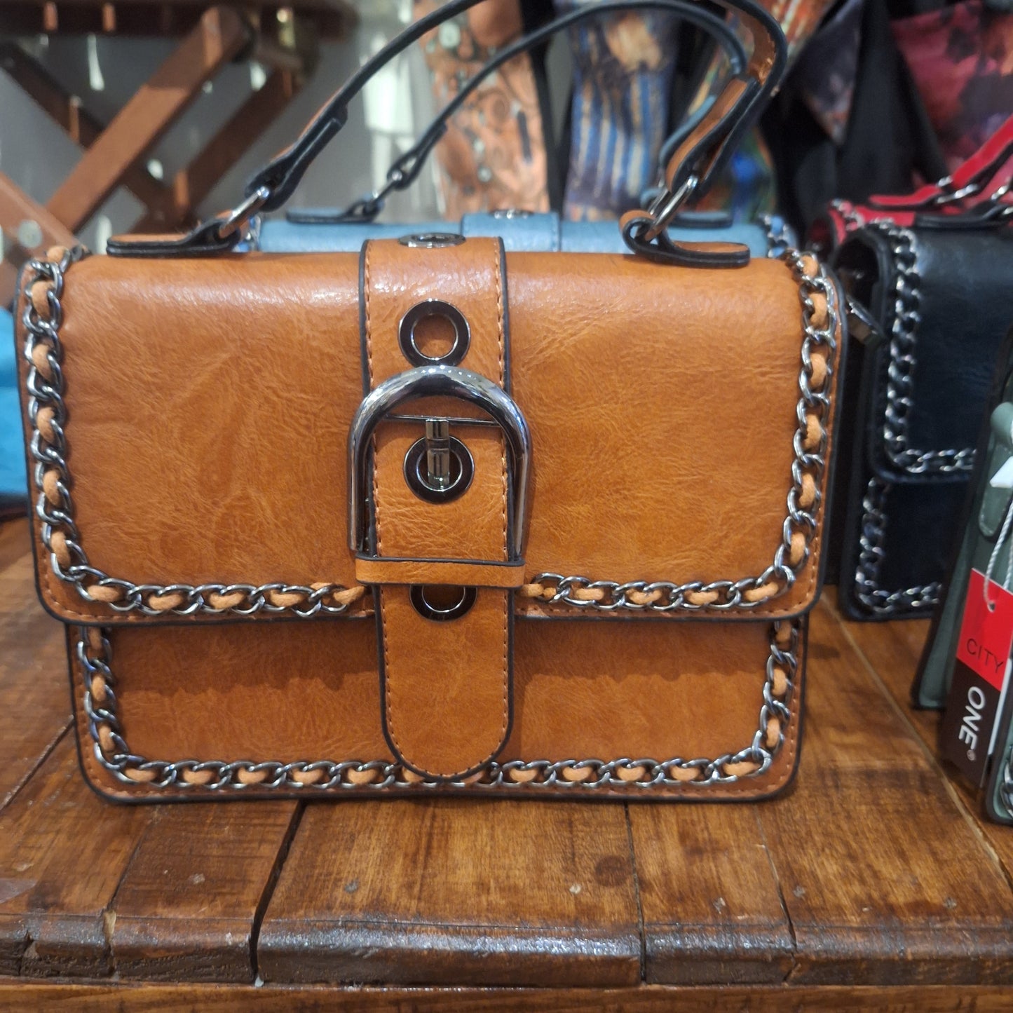 Best selling chain trimmed purse in brown on top of wooden table display