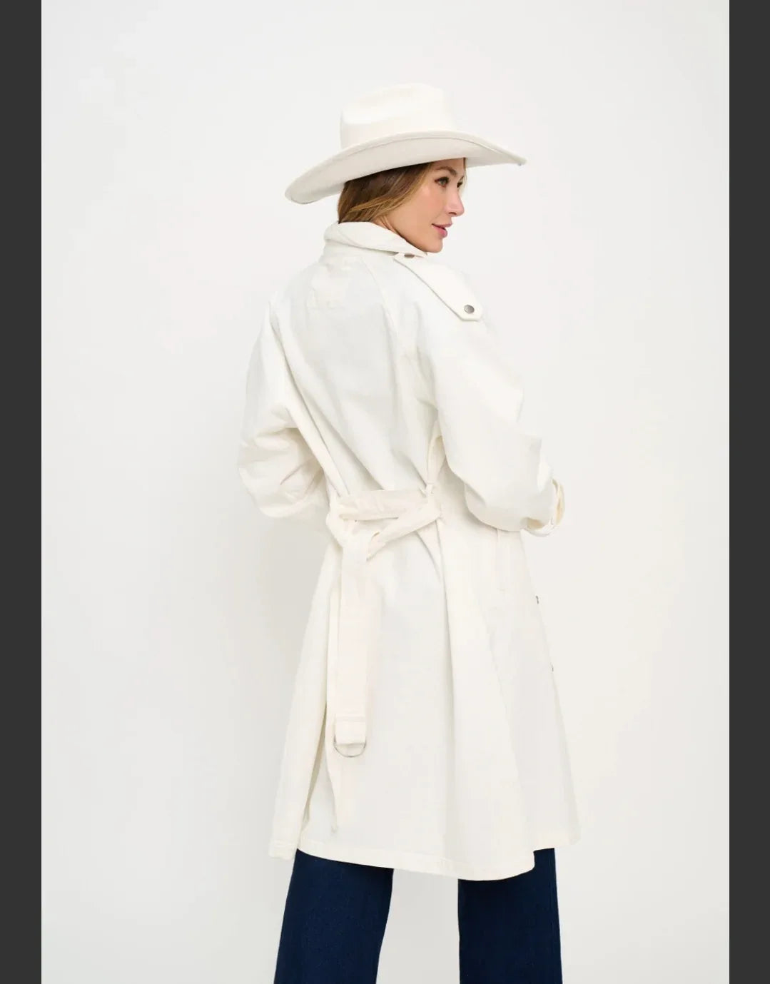 White denim trench coat back/side view with tied belt and buttoned collar tabs