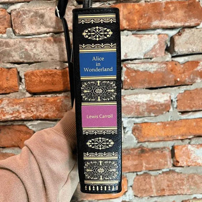 Book-shaped strap with 'Alice in Wonderland' design against a brick wall background