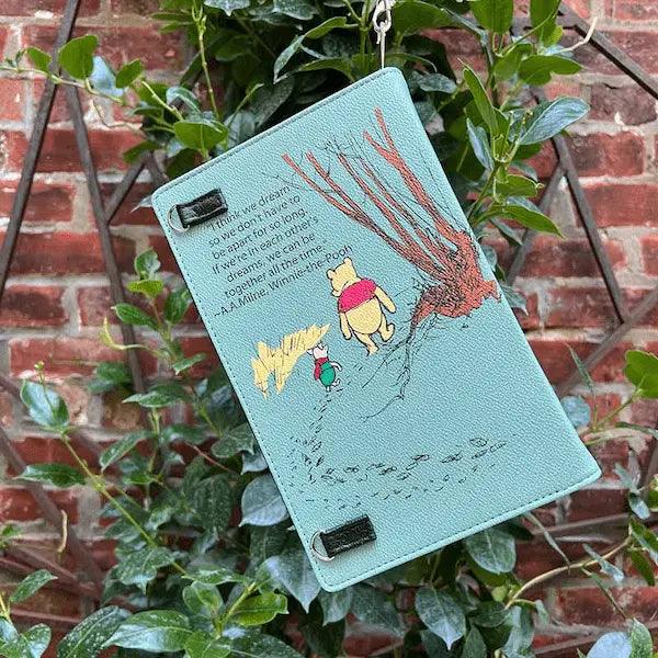  Winnie the Pooh Book Purse hanging on a plant against a brick wall.