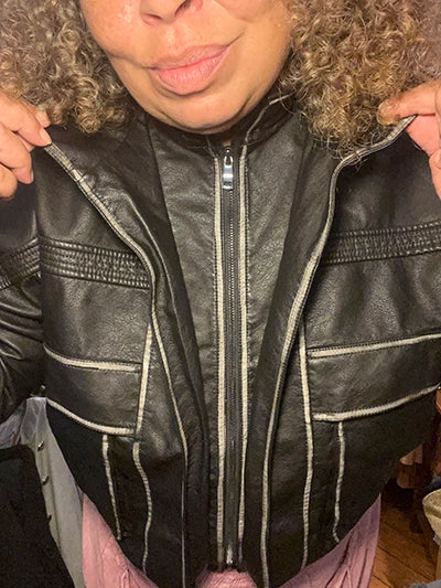Close-up of women's black faux leather biker jacket with silver trim and front zipper