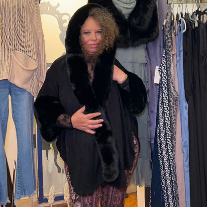 person wearing black cape with hood up , holding fur trim together 