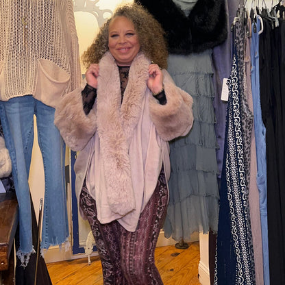 person wearing blush colored cape with hands up holding the faux fur collar 