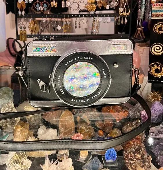 Camera crossbody bag: black body, iridescent lens window, silver trim, shoulder strap