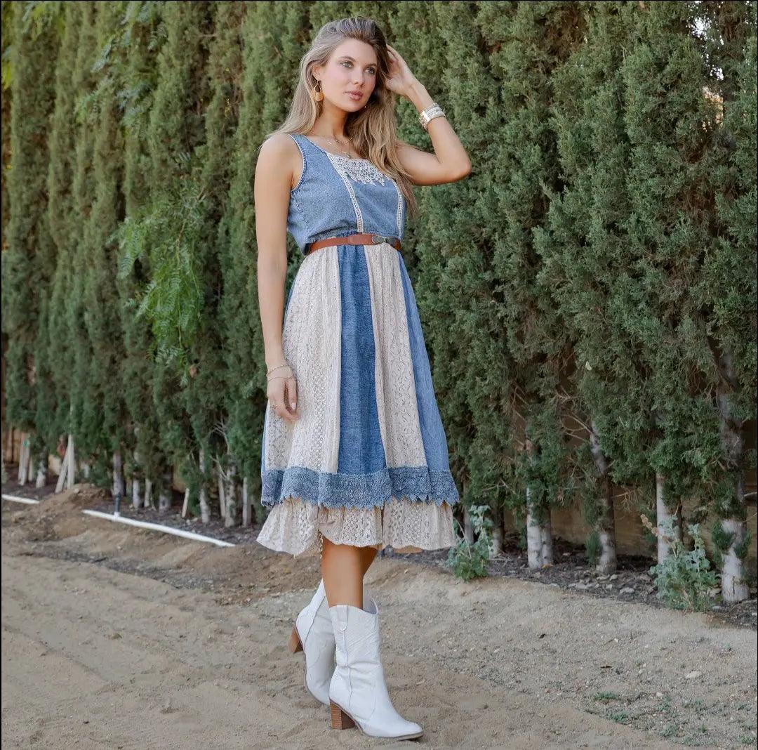 Side view of model wearing the layered denim midi sundress, styled with white boots, outdoors with greenery/trees