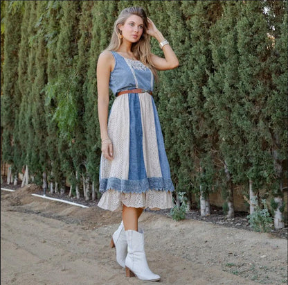Side view of model wearing the layered denim midi sundress, styled with white boots, outdoors with greenery/trees