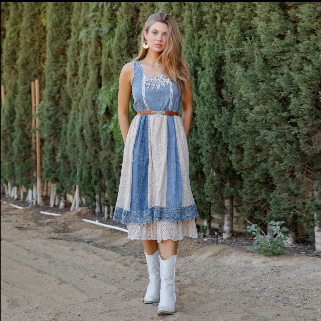Full front view of model wearing the layered denim midi sundress, styled with white boots, outdoors with greenery/trees