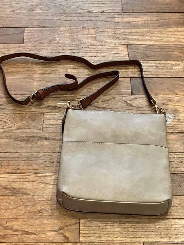 Beige crossbody bag with brown strap on a wooden surface