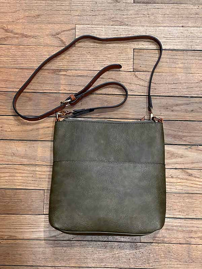 Green leather crossbody bag with brown strap on a wooden surface