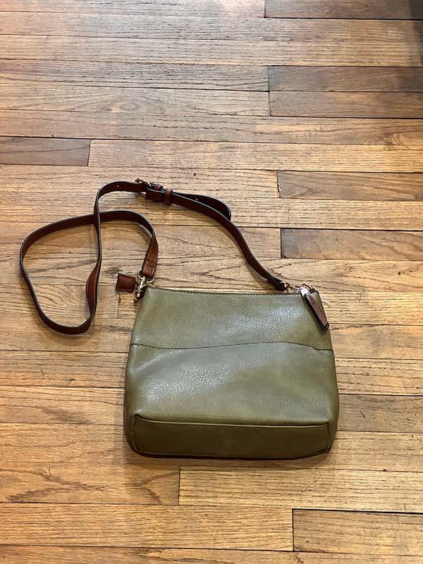 Green leather handbag with brown strap on a wooden floor