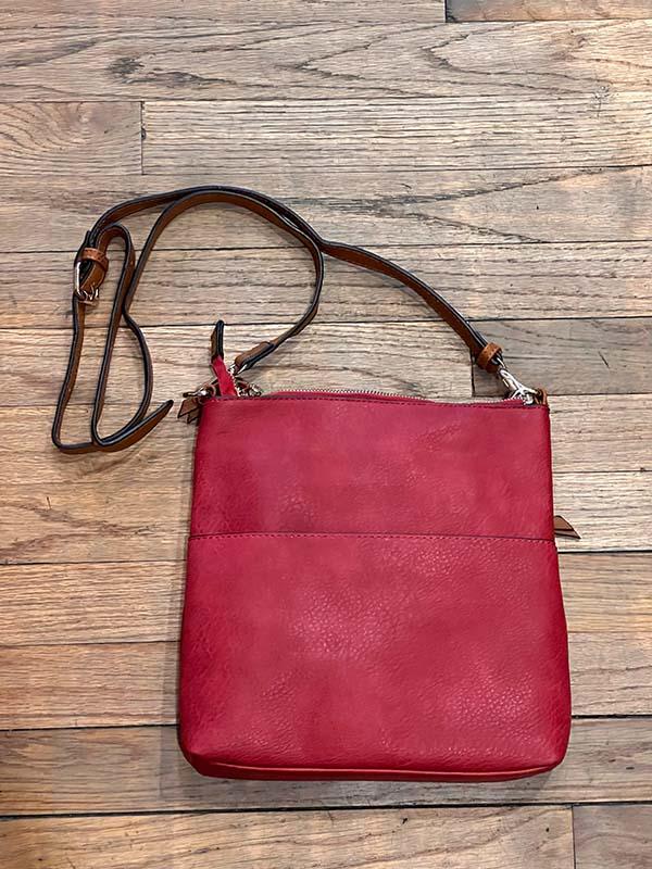 Red leather handbag with brown strap on a wooden surface