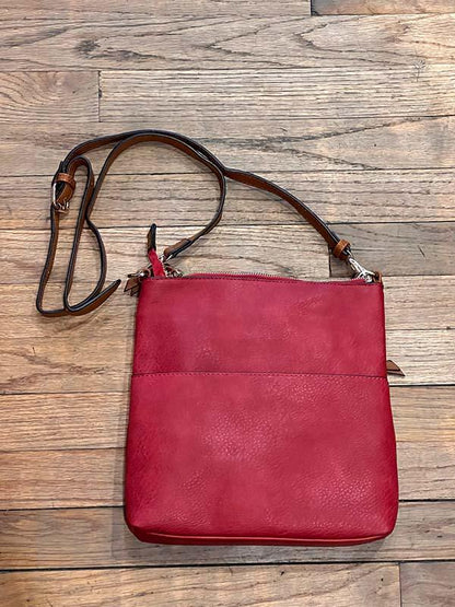 Red leather handbag with brown strap on a wooden surface