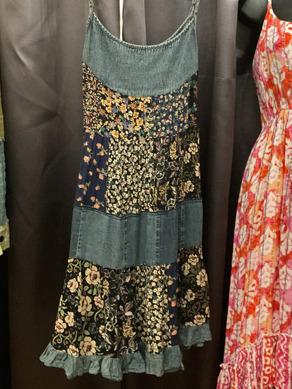 A new arrival summer dress built to be size inclusive and featurin soft denim, patchwork and ruffles,  hanging from the dressing room. 