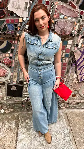 Light blue denim jumpsuit with sleeveless collared bib and button front, wide leg.