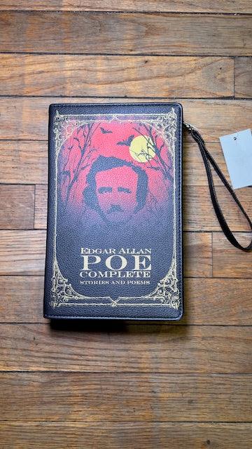 A purse designed like the Book titled 'The Complete Works of Edgar Allan Poe' on a wooden surface