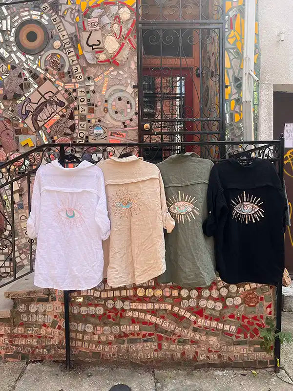Four linen shirts on hangers in front of a colorful mosaic wall.
