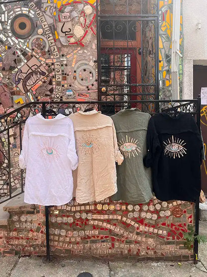 Four linen shirts on hangers in front of a colorful mosaic wall.
