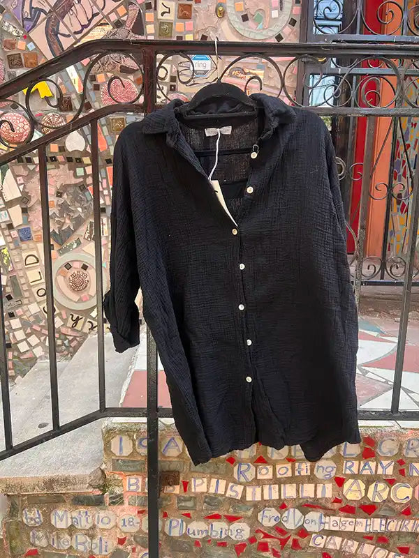 Black linen shirt on a hanger against a colorful mosaic wall.