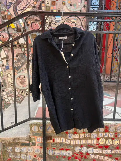 Black linen shirt on a hanger against a colorful mosaic wall.