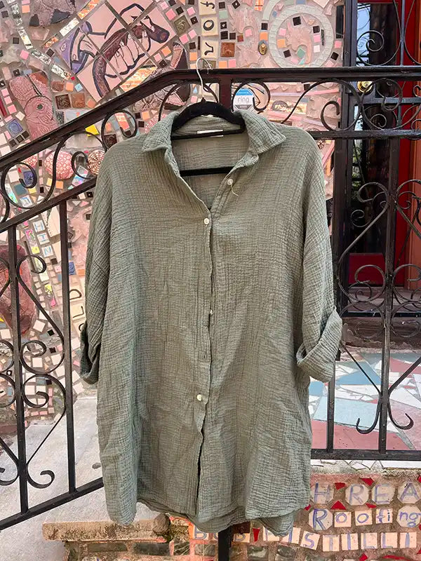 Green button-up shirt on a hanger with a mosaic wall background