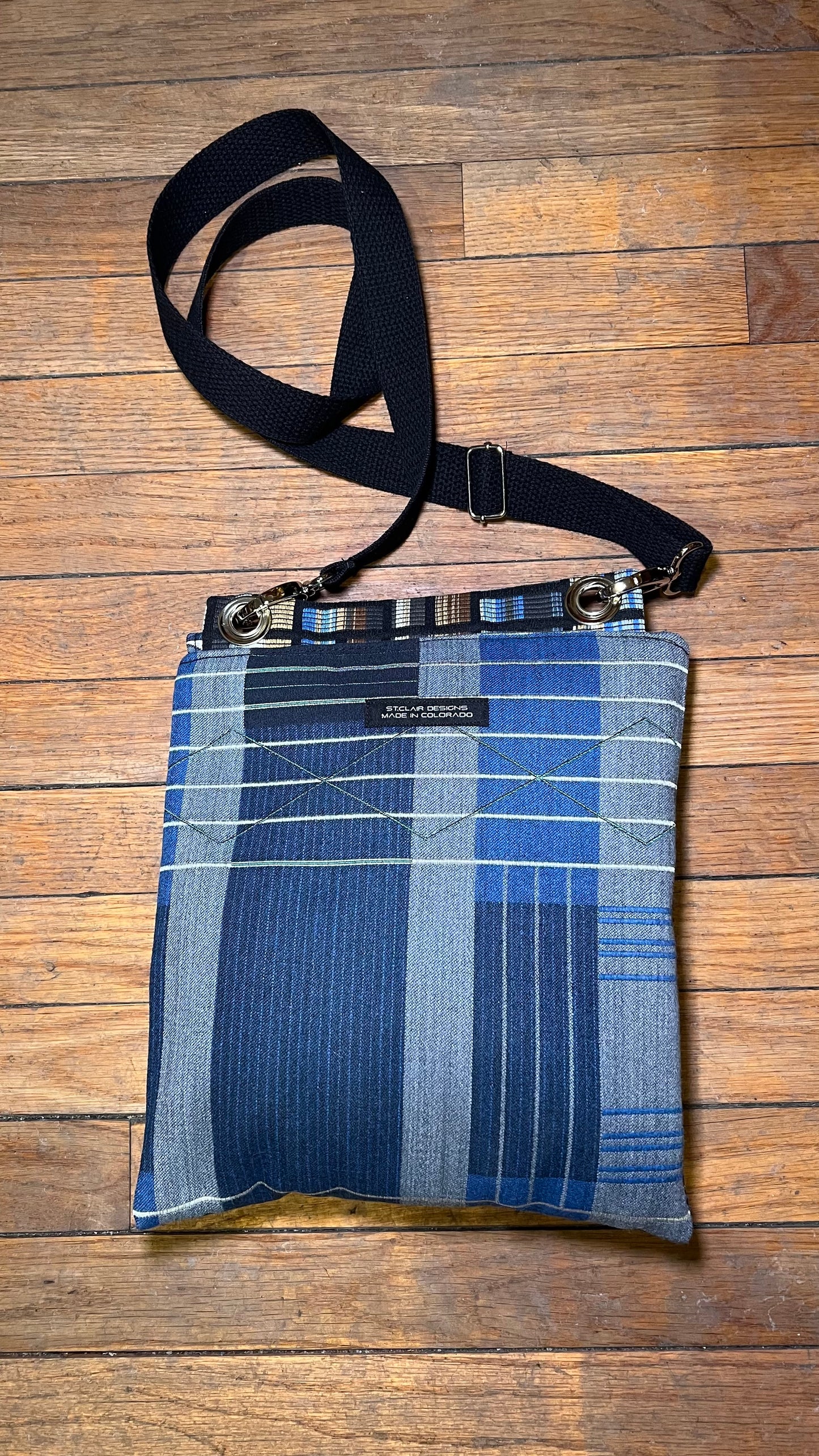 Blue plaid bag with a black strap on a wooden surface