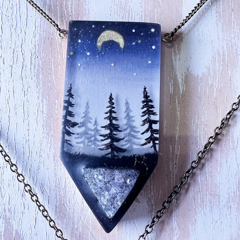 Necklace with a pendant featuring a night sky with trees and a moon.