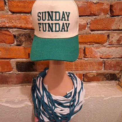 Mannequin wearing a cap with 'SUNDAY FUNDAY' text  and a shredded green and white scarf for Eagles Football Day against a brick wall.