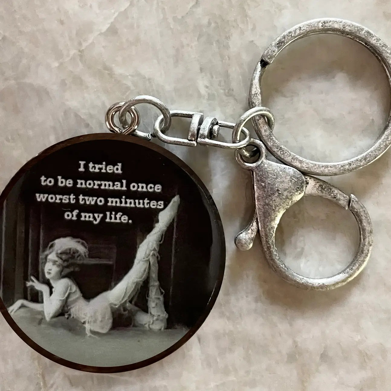 Keychain with black circular pendant featuring a black and white illustration and text on a beige surface.
