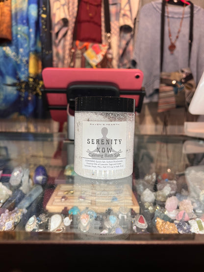 Bottle of 'Serenity Now' balm in a store setting with jewelry and clothing in the background