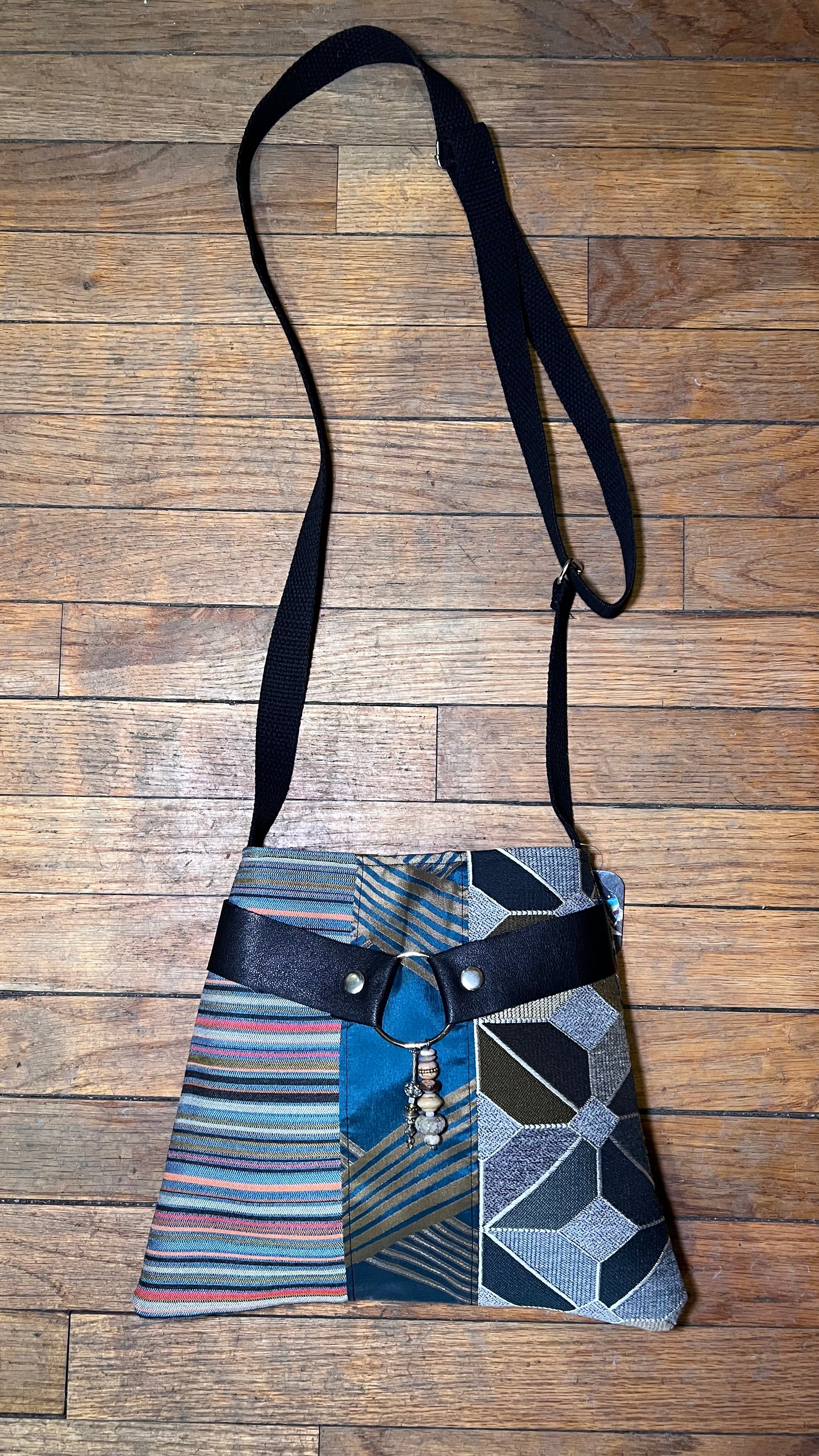 Multicolored patterned bag with a black strap on a wooden surface