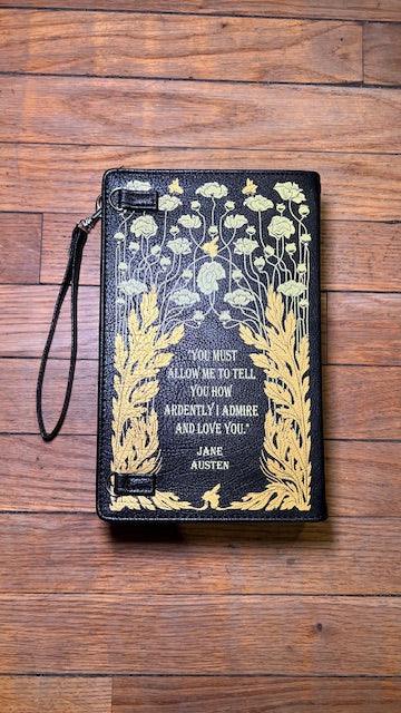 Black clutch with gold floral design  and  Jane Austen quote and text on a wooden surface