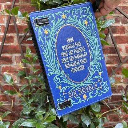 Blue storybook purs featuring the 6 novels of jane austen with literary design against a brick wall and plant background