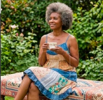 Woman sitting outdoors holding a cup, surrounded by greenery wearing a trendy bohemian style patchwork dress for women featuring mixed floral prints and a tiered silhouette. A unique boutique find that pairs a flowy fit with a ruffled trim for a chic, effortless summer look.