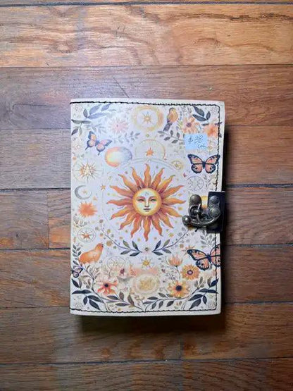 Spiritual journal cover with sun face, butterflies, and floral motifs, metal clasp on right
