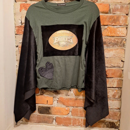 Custom Philadelphia Eagles Game Day poncho hanging on a brick wal. Velvet arms and aplique heart. the main body is an olive t shirt with a sparkly Eagles Football patch.