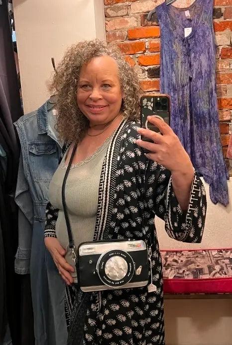 Camera crossbody bag worn crossbody, black-and-silver camera-style front with lens window