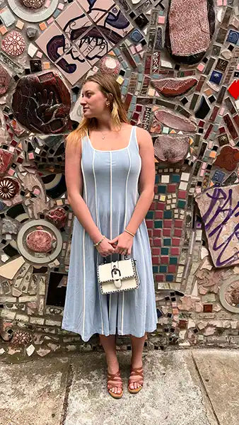 Woman in a light blue dress standing in front of a mosaic wall.