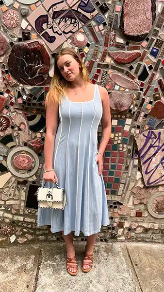 Woman in a light blue dress standing in front of a mosaic wall.