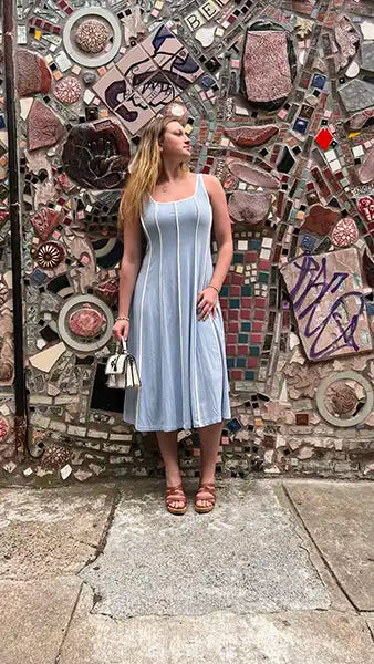 Woman in a light blue dress standing in front of a mosaic wall.