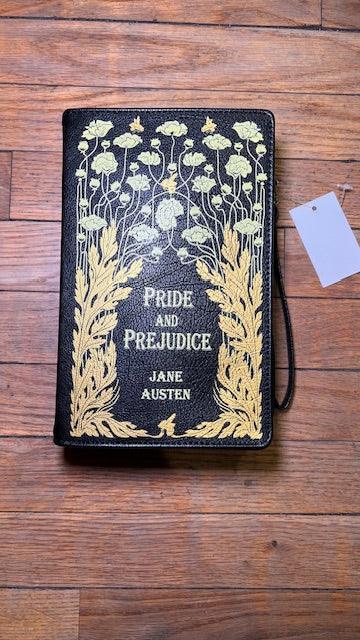 'Pride and Prejudice' by Jane Austen book cover is designed as a wristlet and crossbody handbag with floral design on a wooden surface