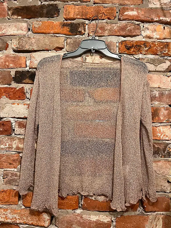 Beige textured shrug with open front, long sleeves, and scalloped hem edge.