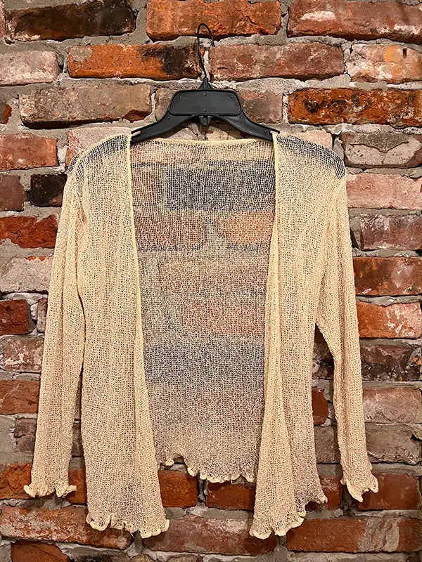 Cream textured shrug with open front, long sleeves, and scalloped hem edge.