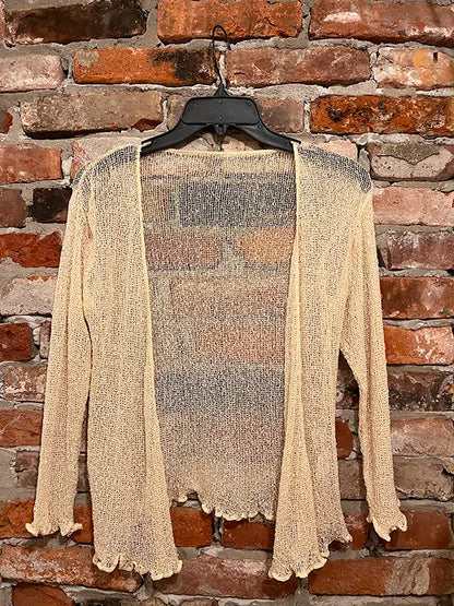 Cream textured shrug with open front, long sleeves, and scalloped hem edge.