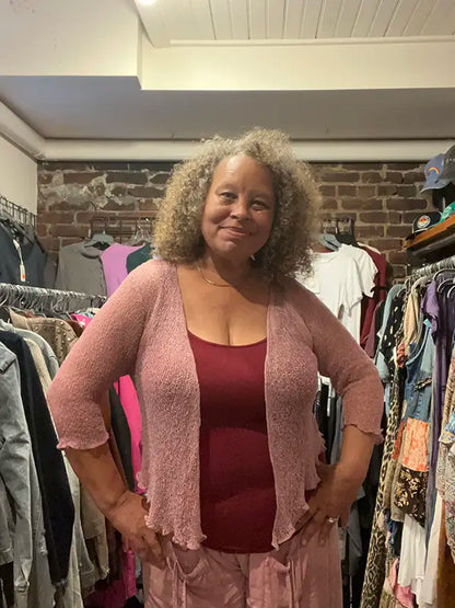 Mauve knitted shrug on model with open front, 3/4 sleeves, and scalloped hem.