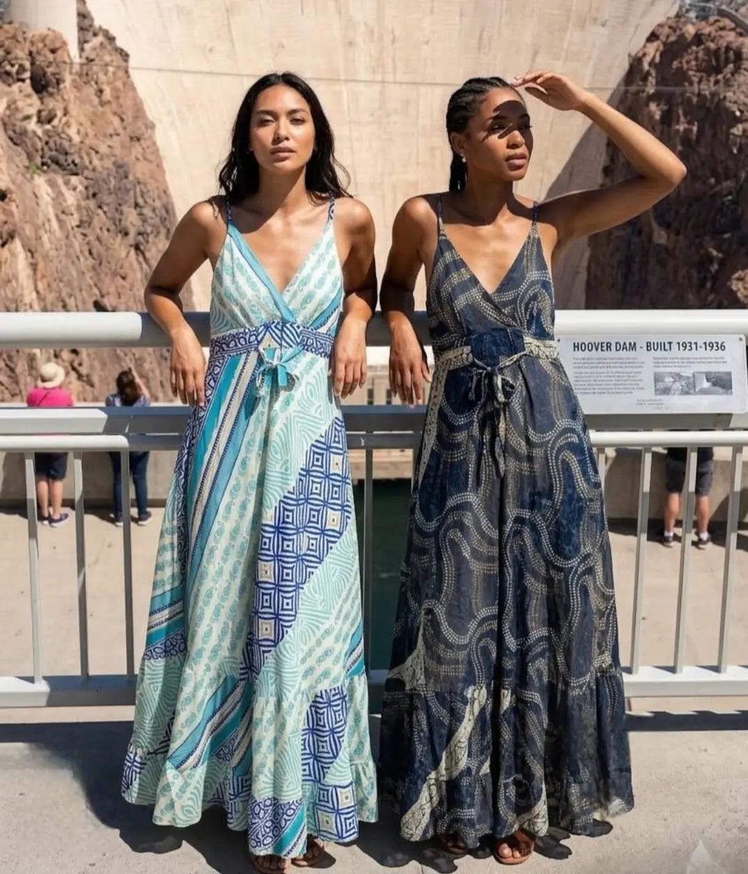 wo women wearing the Sari Maxi Dress in aqua patchwork geometric print and navy dotted swirl print, leaning against a railing at Hoover Dam.